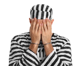 Photo of Remorseful prisoner in striped uniform with handcuffs hiding his face on white background