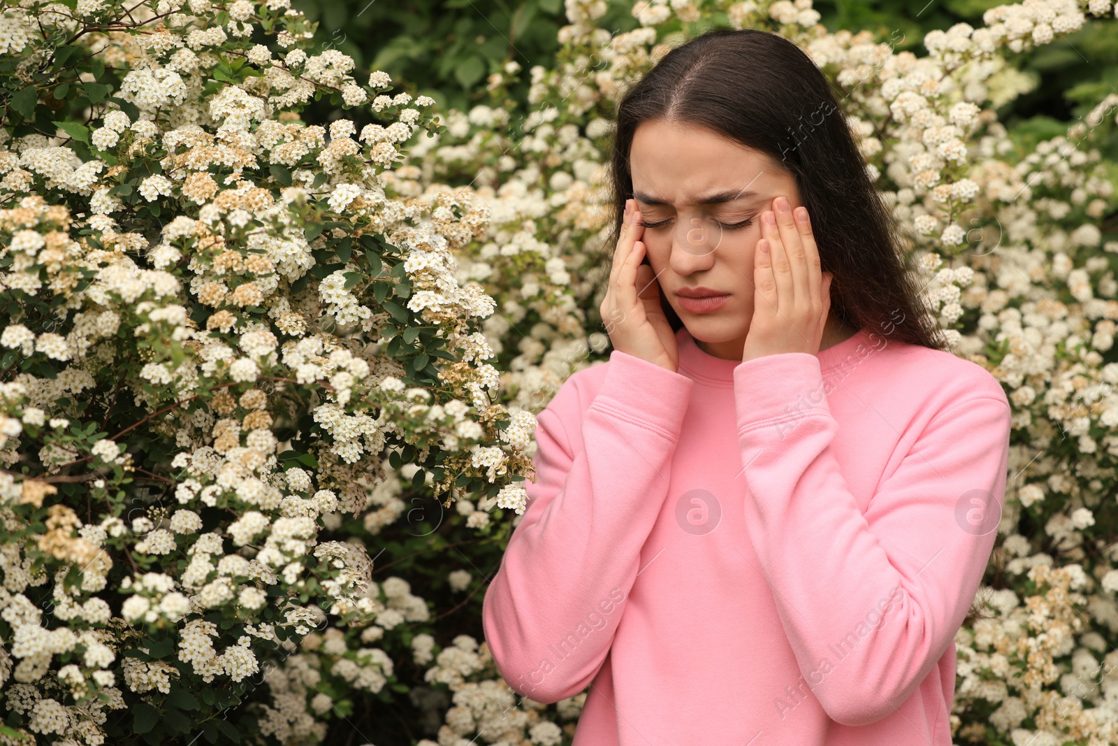 Photo of Woman suffering from seasonal pollen allergy near blossoming tree on spring day