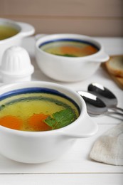 Delicious chicken bouillon with carrot and parsley on white wooden table, closeup