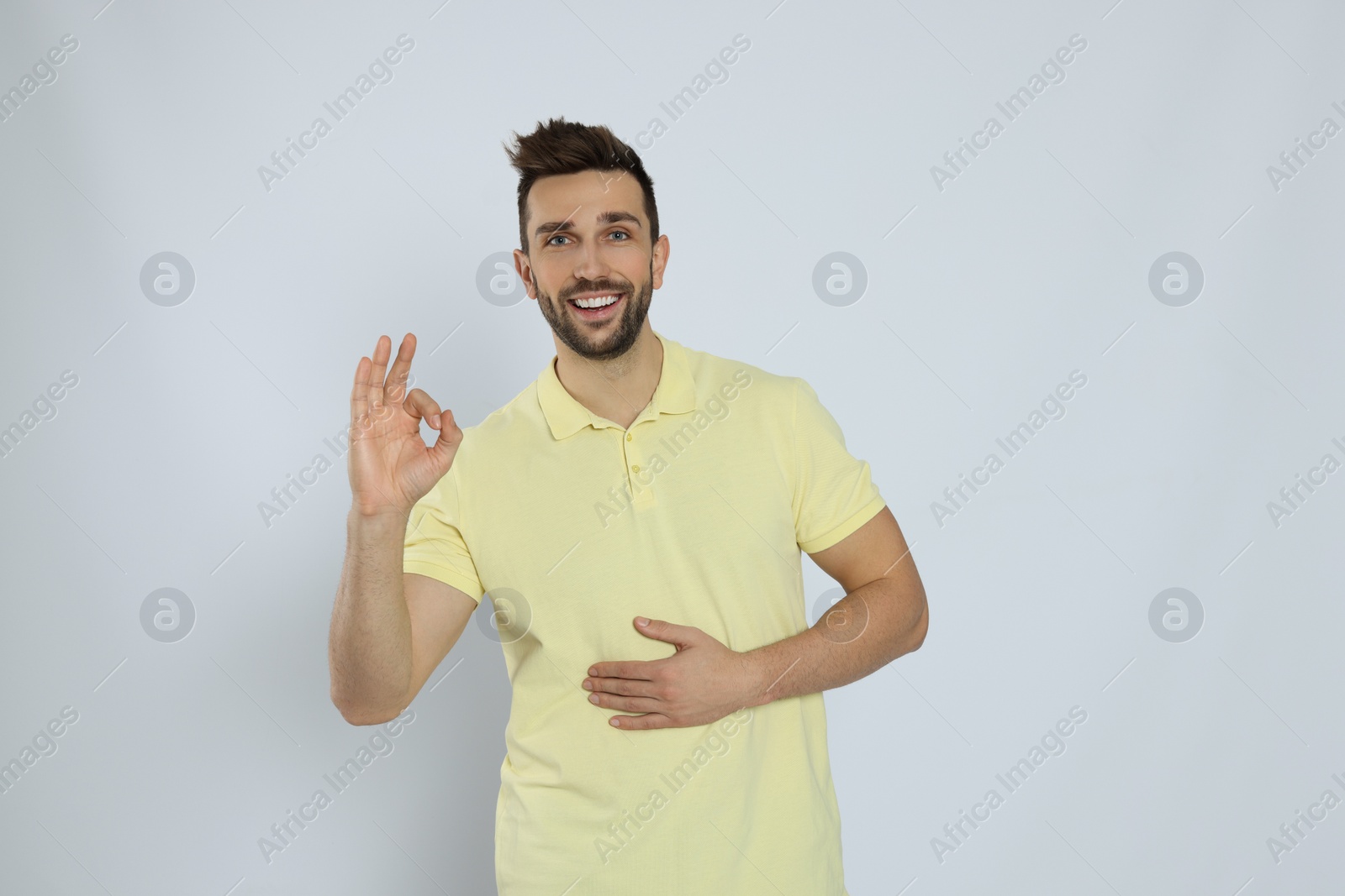Photo of Happy man touching his belly and showing okay gesture on light background. Concept of healthy stomach