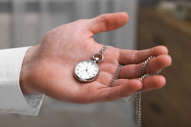 Photo of Man holding chain with elegant pocket watch on blurred background, closeup