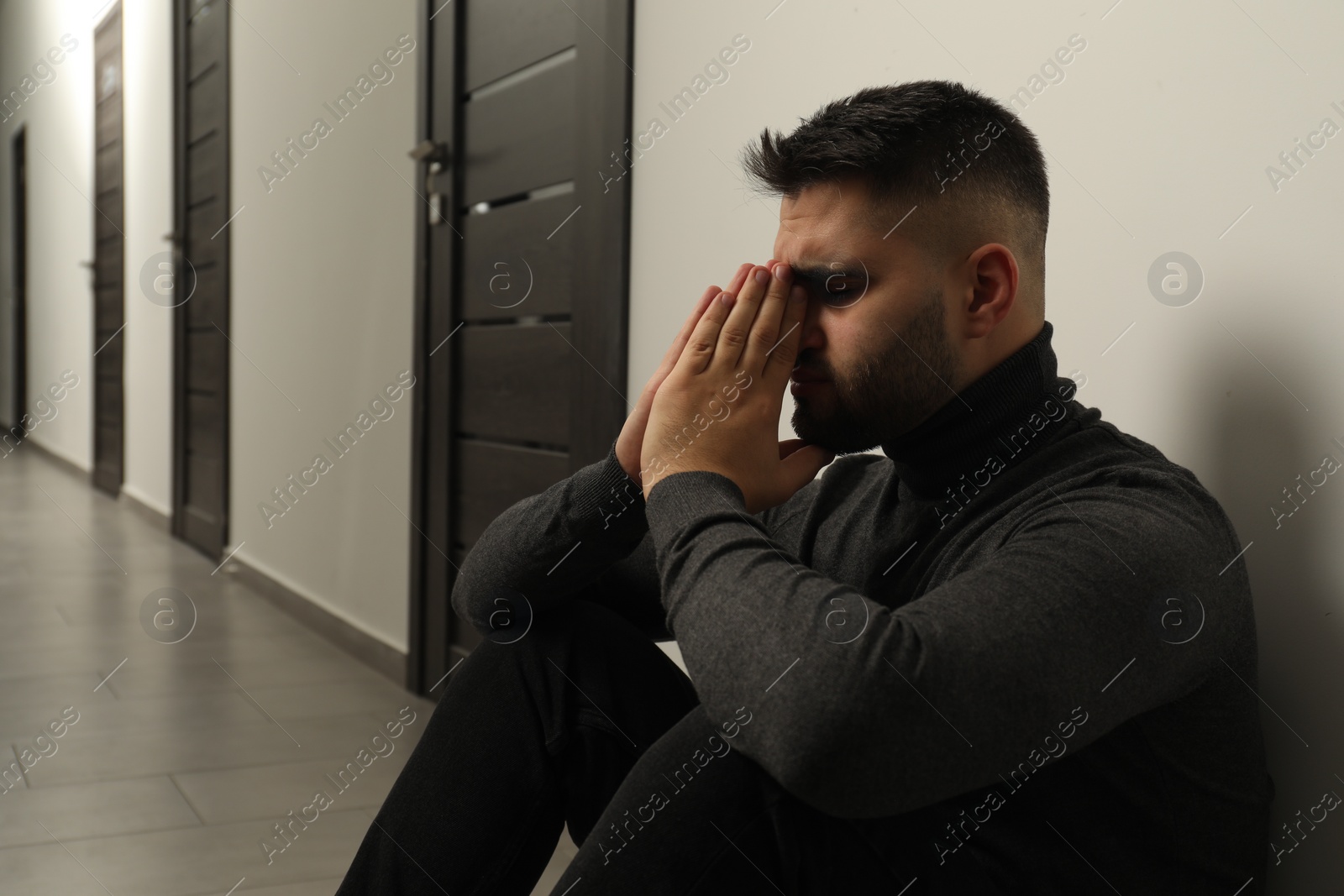 Photo of Sad man sitting on floor in hall. Space for text