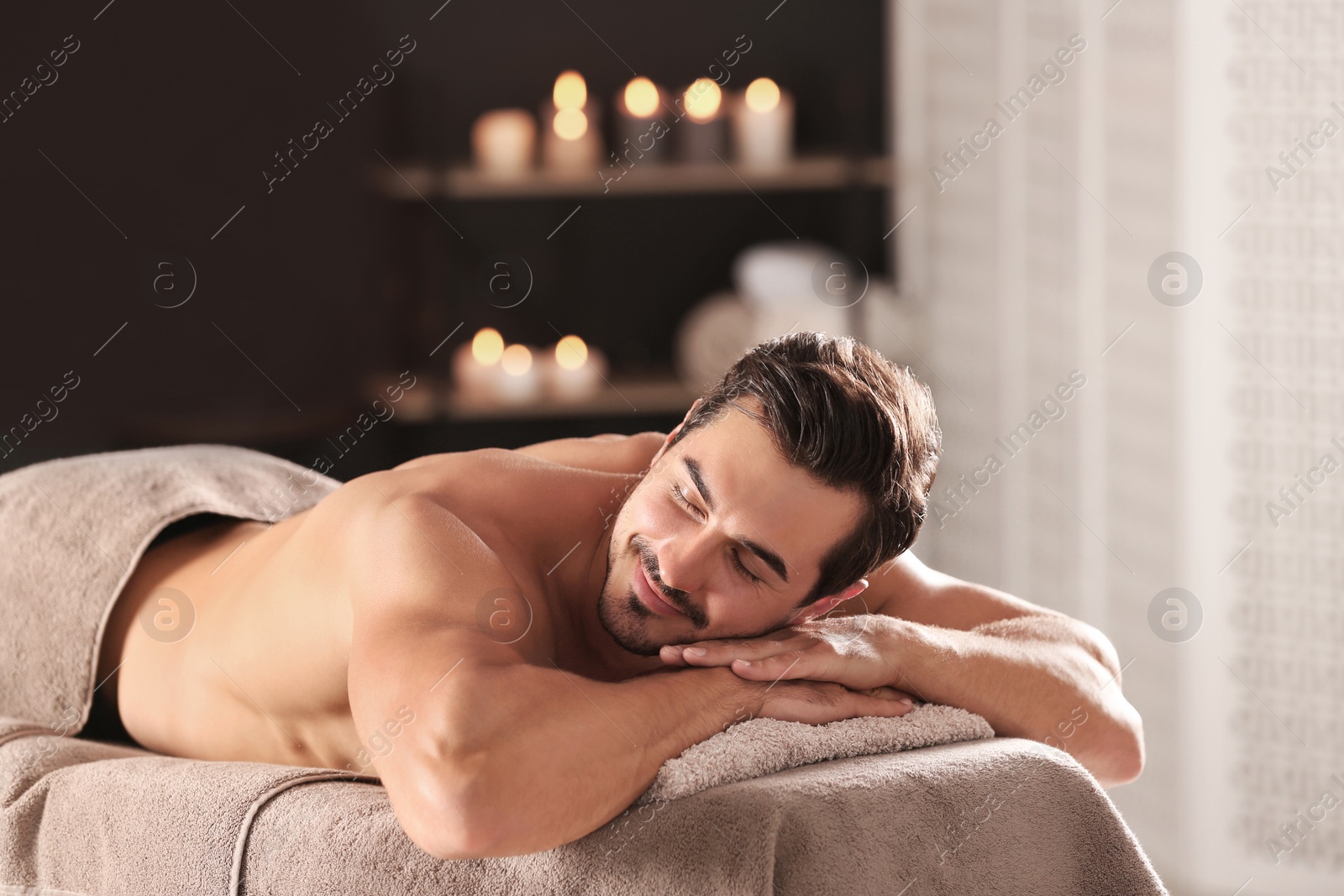 Photo of Handsome young man relaxing on massage table in spa salon, space for text