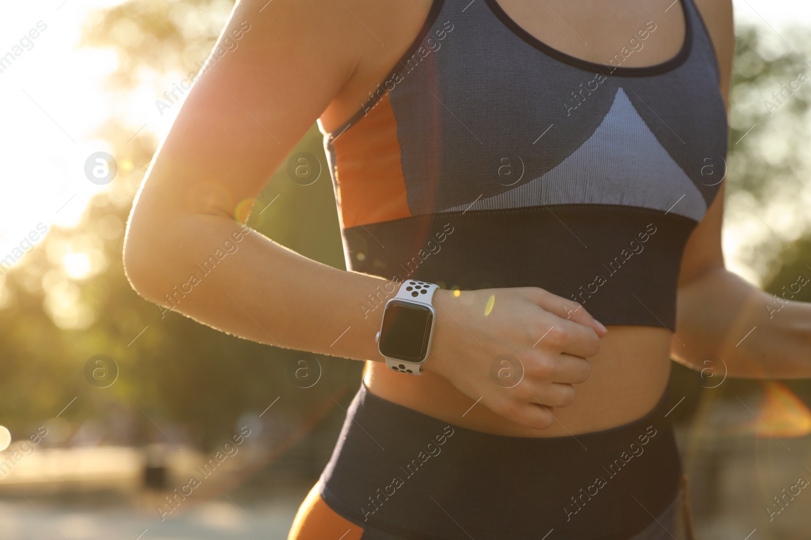 Photo of Woman wearing modern smart watch during training outdoors, closeup