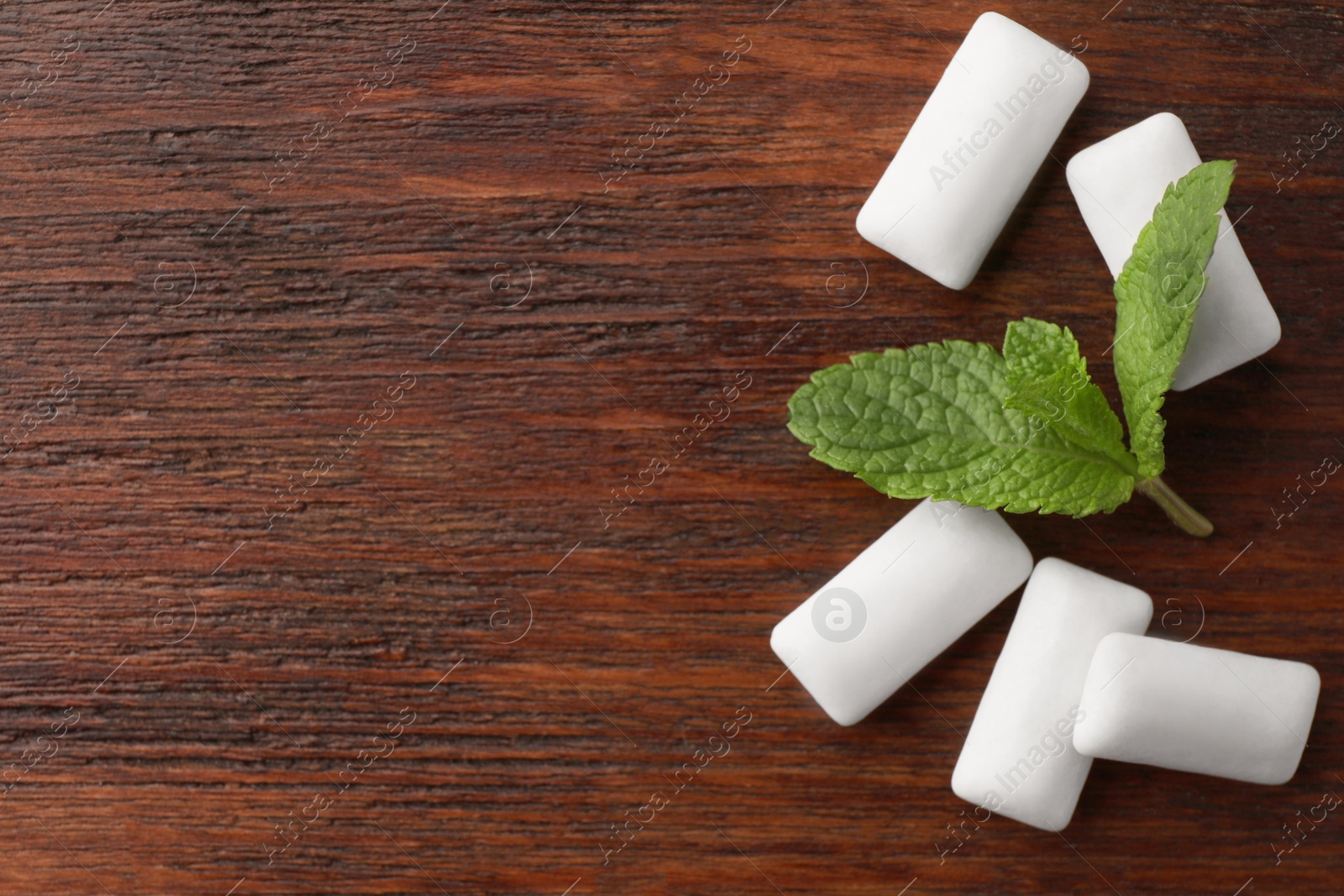 Photo of Tasty white chewing gums and mint leaves on wooden table, flat lay. Space for text