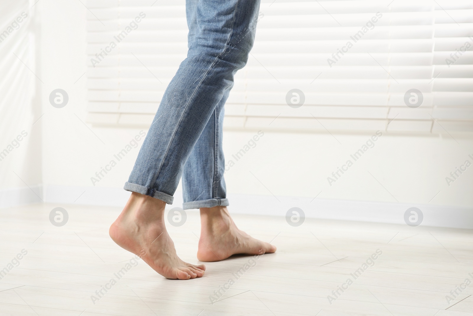 Photo of Barefoot woman walking on white parquet at home, closeup. Heated floor