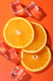 Slices of juicy orange and ice cubes on terracotta background, flat lay