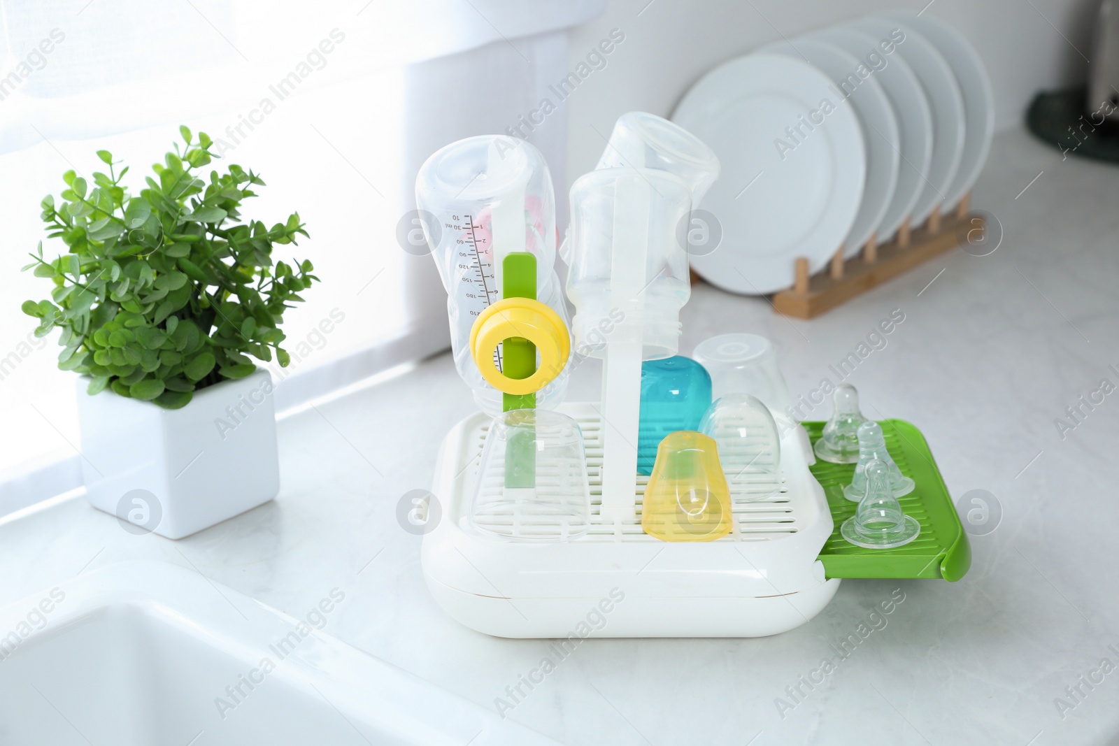 Photo of Dryer with baby bottles and nipples after sterilization on white countertop in kitchen