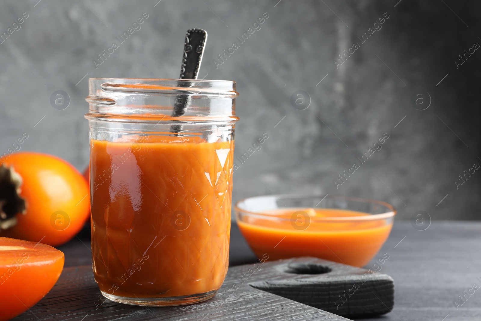 Photo of Delicious persimmon jam in glass jar served on dark gray wooden table, space for text