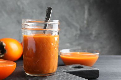 Delicious persimmon jam in glass jar served on dark gray wooden table, space for text