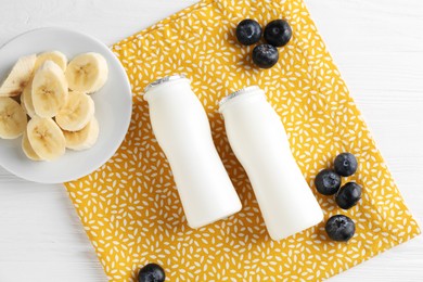 Tasty yogurt in bottles, banana and blueberries on white wooden table, top view