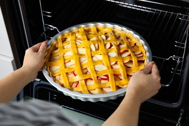 Woman putting raw traditional English apple pie into oven, closeup