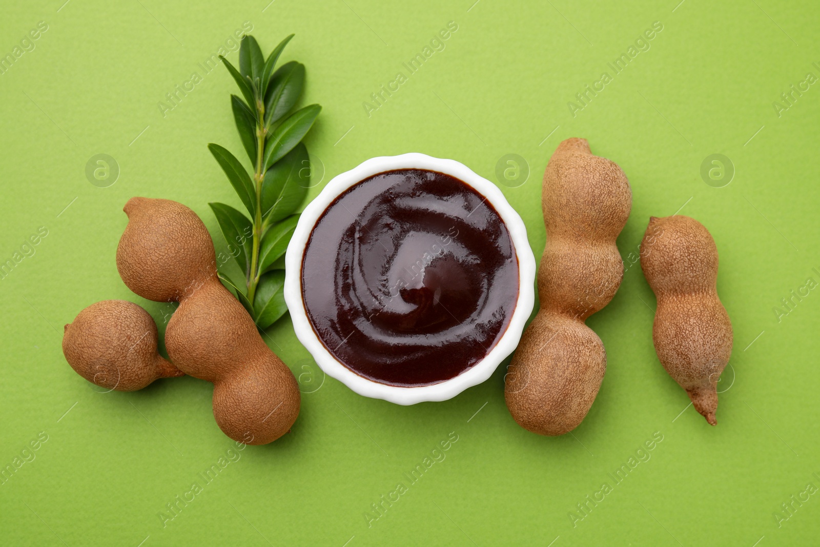 Bowl of tasty tamarind sauce, leaves and fresh pods on light green table, flat lay Photo of Bowl of tasty tamarind sauce, leaves and fresh pods on light green table, flat lay