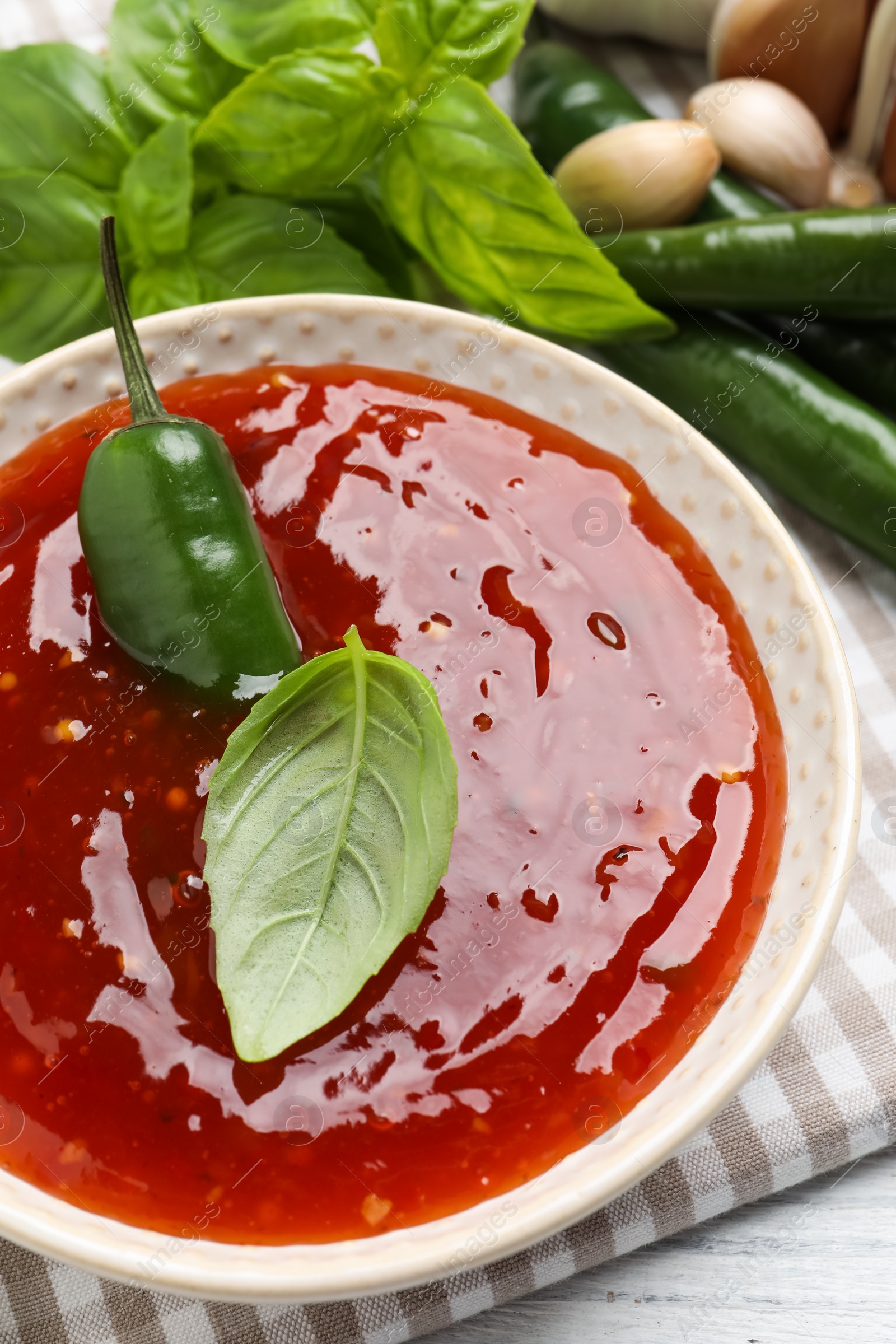 Photo of Spicy chili sauce with basil on white table, closeup