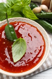 Photo of Spicy chili sauce with basil on white table, closeup