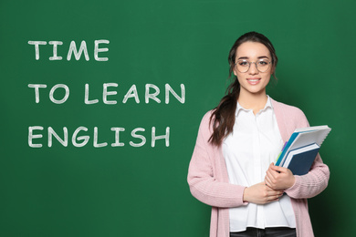 Beautiful teacher near green chalkboard with text Time To Learn English