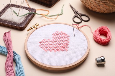 Photo of Embroidery and different sewing accessories on beige background