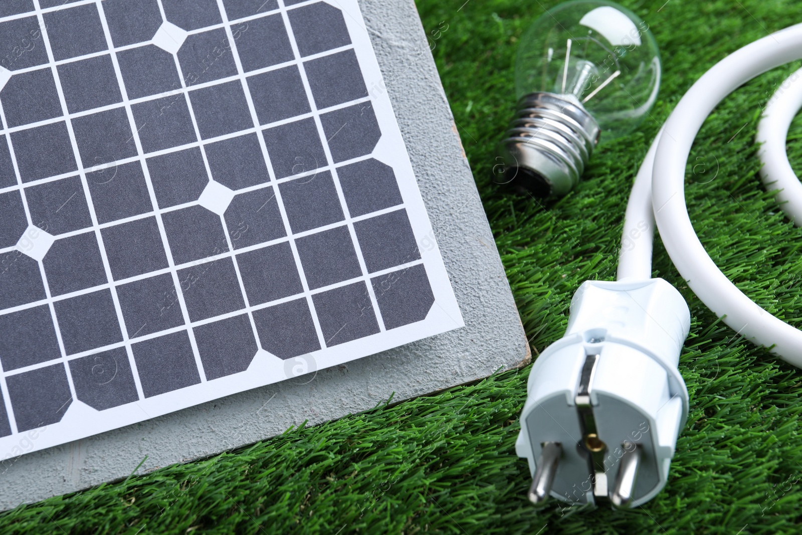 Photo of Solar panel, cable and light bulb on green grass, closeup