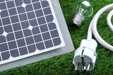 Photo of Solar panel, cable and light bulb on green grass, closeup