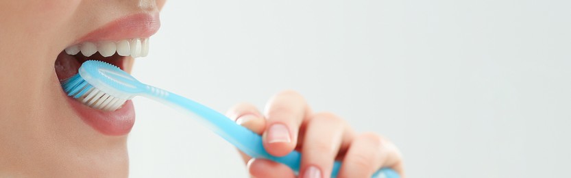 Woman brushing her teeth with plastic toothbrush on white background, closeup. Banner design with space for text