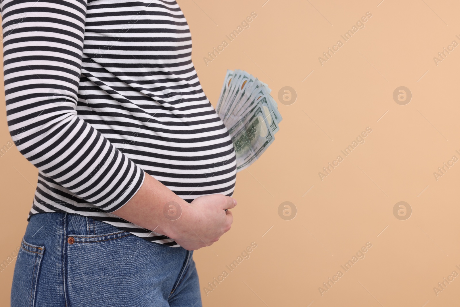 Photo of Surrogate mother. Pregnant woman with dollar banknotes on beige background, closeup. Space for text