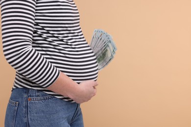 Surrogate mother. Pregnant woman with dollar banknotes on beige background, closeup. Space for text