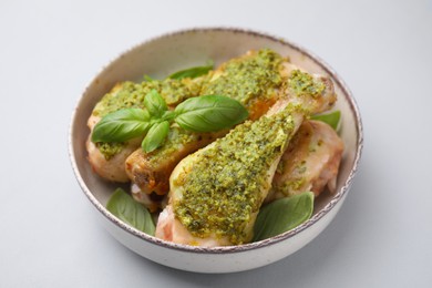 Delicious fried chicken drumsticks with pesto sauce and basil in bowl on light gray table, closeup