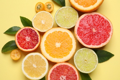 Photo of Fresh juicy citrus fruits with green leaves on light yellow background, flat lay