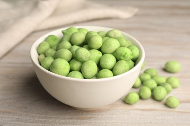 Bowl with tasty wasabi coated peanuts on white wooden table, closeup