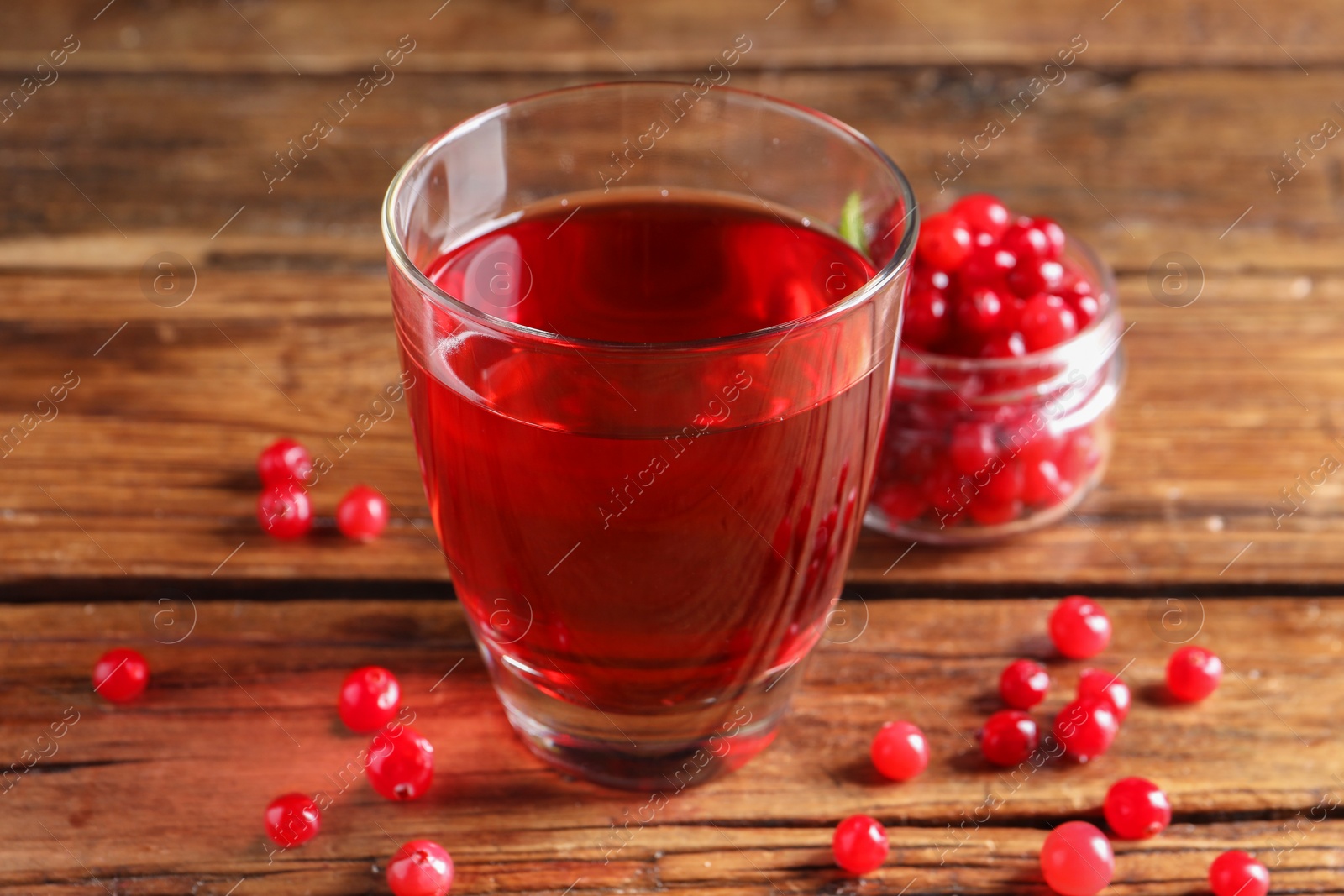 Photo of Tasty cranberry juice in glass and fresh berries on wooden table, closeup