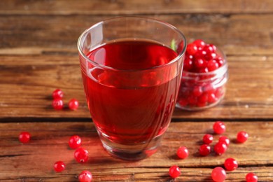 Photo of Tasty cranberry juice in glass and fresh berries on wooden table, closeup