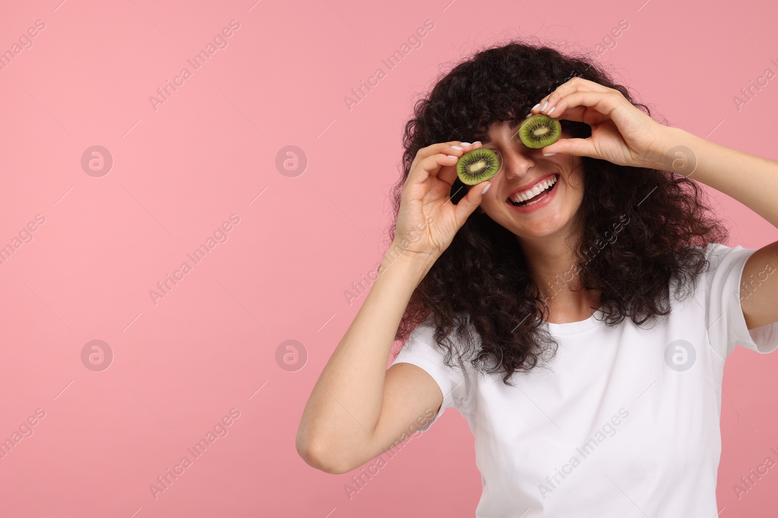 Photo of Woman covering eyes with halves of kiwi on pink background, space for text