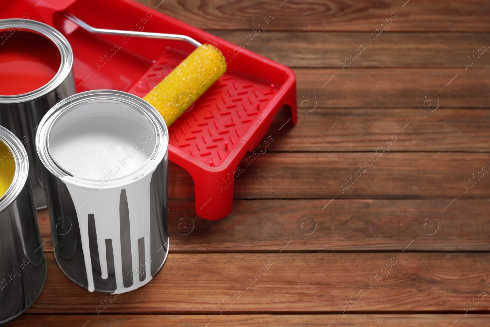 Photo of Cans of paints, roller and tray on wooden table, space for text