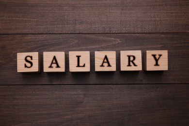 Image of Word Salary made with cubes on wooden table, flat lay