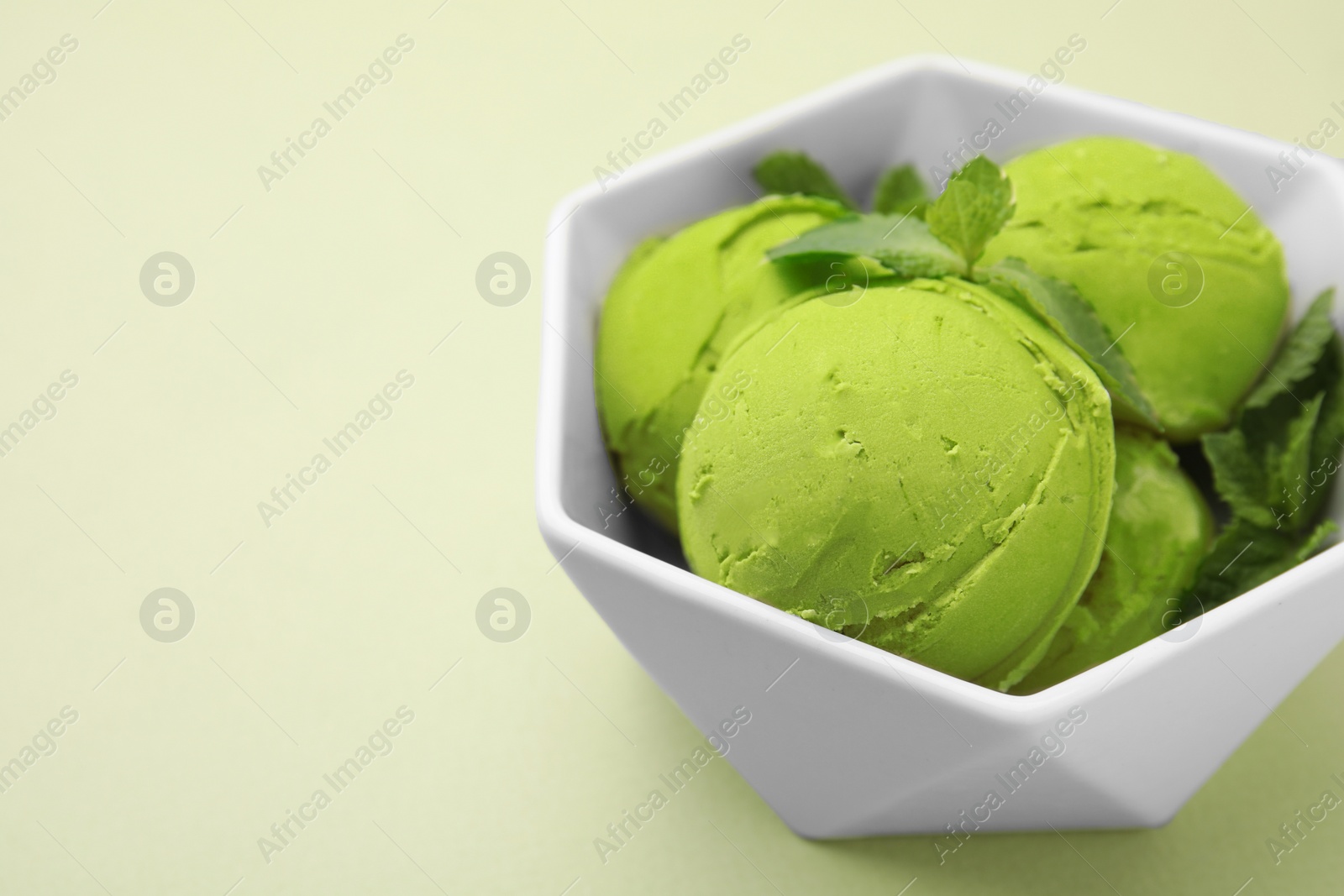 Photo of Tasty matcha ice cream with mint in bowl on pale green background, closeup. Space for text