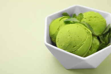 Photo of Tasty matcha ice cream with mint in bowl on pale green background, closeup. Space for text