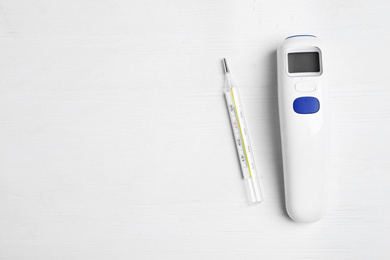 Photo of Non-contact infrared and mercury thermometers on white wooden background, flat lay. Space for text