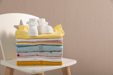 Photo of Stack of baby clothes and booties on chair near beige wall. Space for text