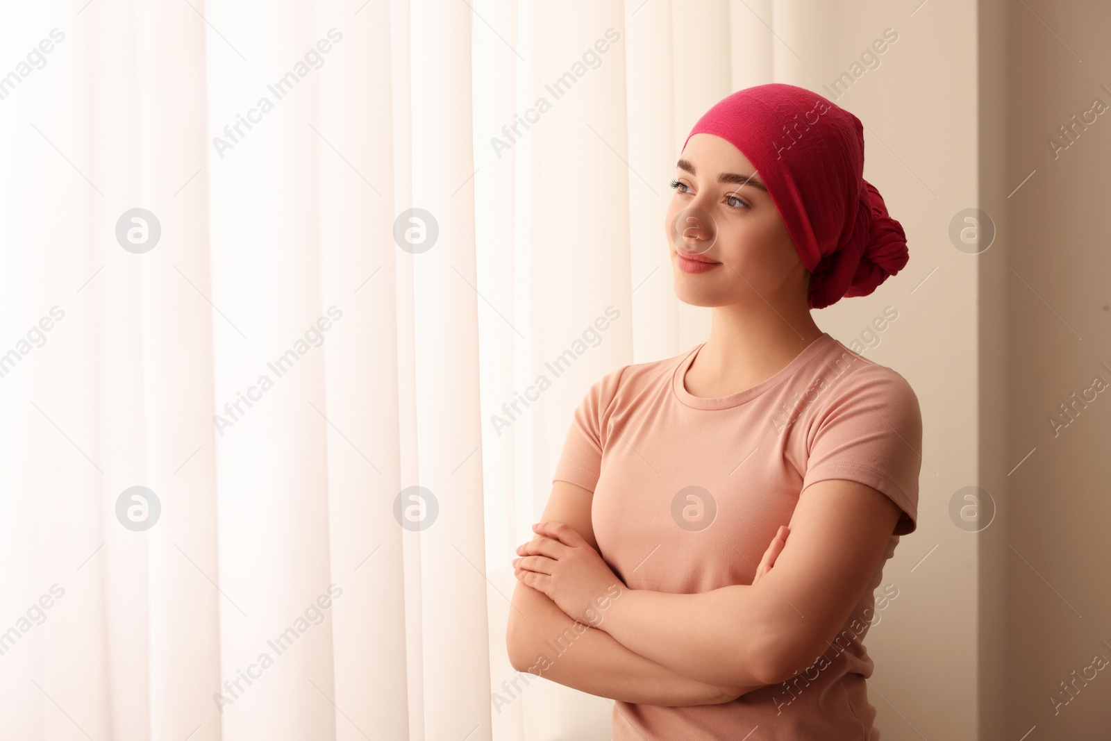 Photo of Cancer patient. Young woman with headscarf near window indoors, space for text