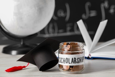 Photo of Scholarship concept. Glass jar with coins and graduation cap on white wooden table