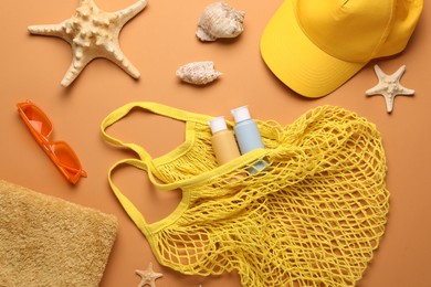 String bag and different beach accessories on pale orange background, flat lay