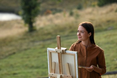 Photo of Beautiful young woman drawing on canvas in nature. Space for text