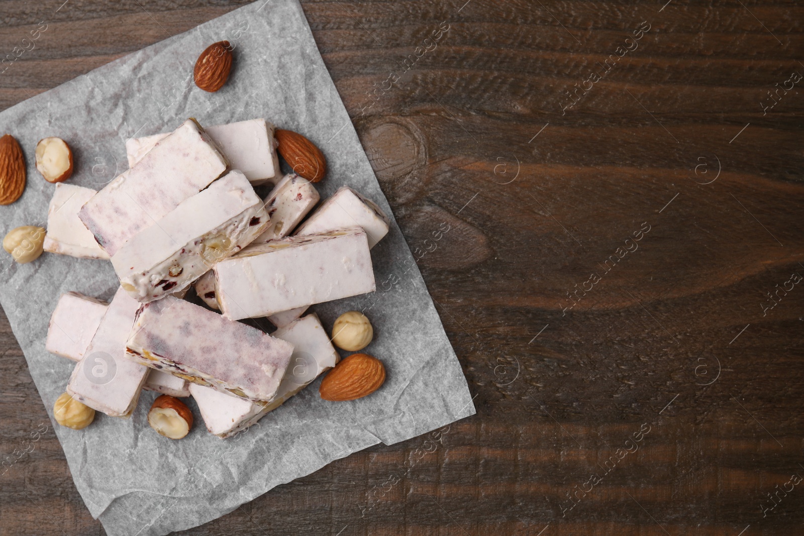 Photo of Pieces of delicious nutty nougat, hazelnuts and almonds on wooden table, top view. Space for text