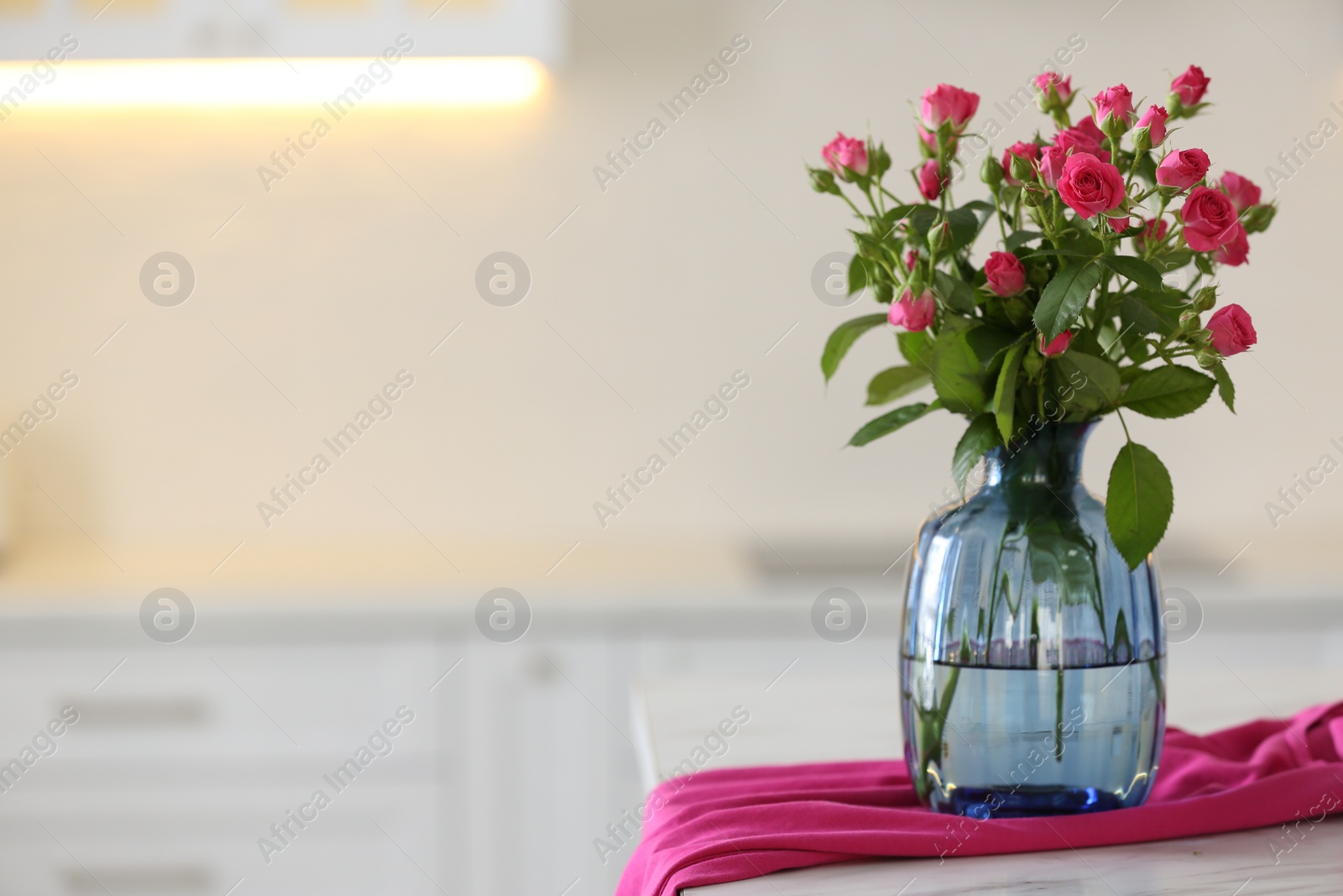 Photo of Glass vase with fresh flowers and towel on table in kitchen. Space for text