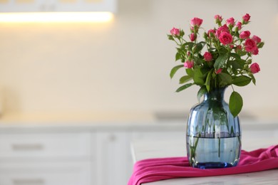 Glass vase with fresh flowers and towel on table in kitchen. Space for text