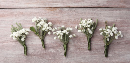 Photo of Many small stylish boutonnieres on light wooden table, flat lay