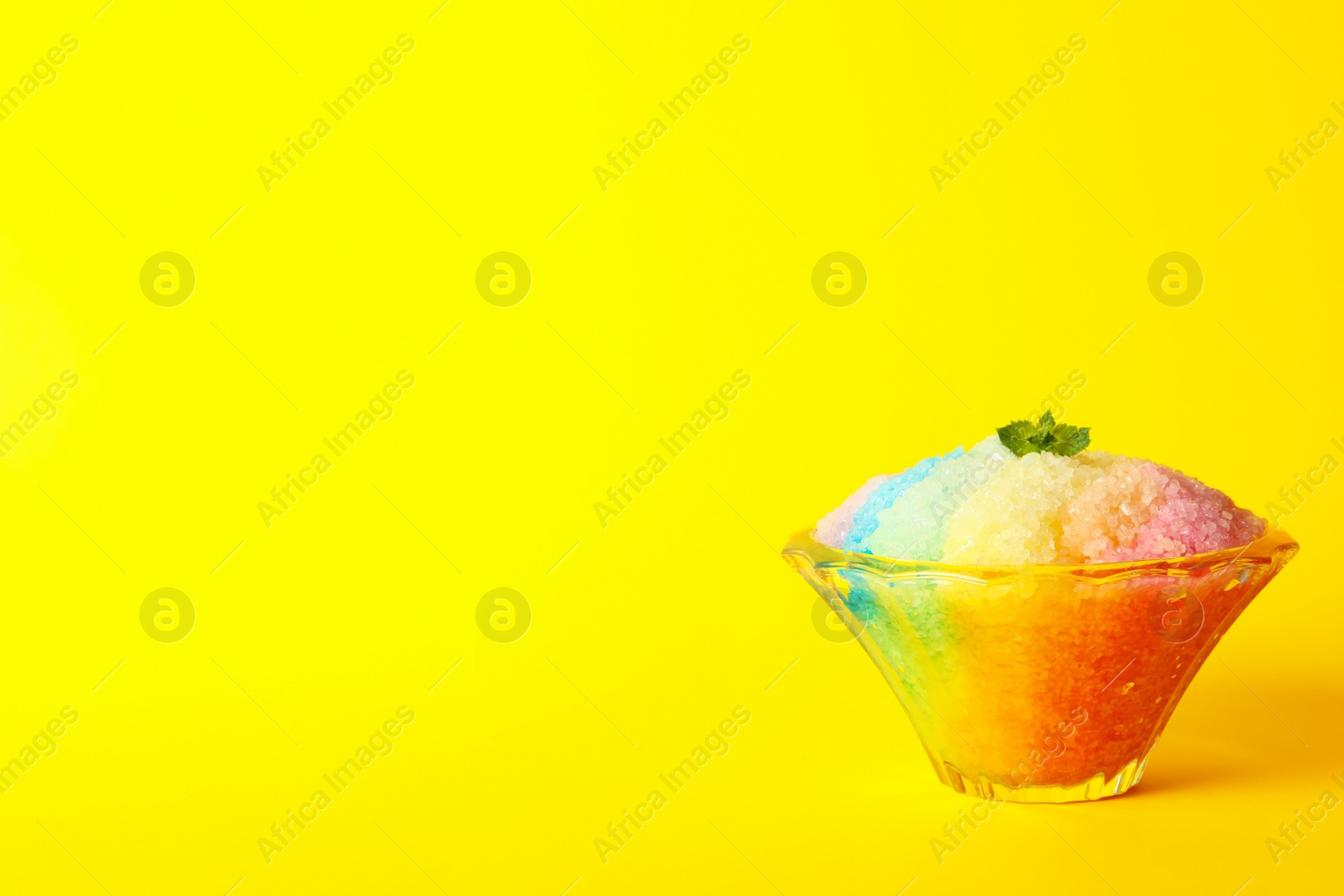 Photo of Rainbow shaving ice in glass dessert bowl on yellow background, space or text