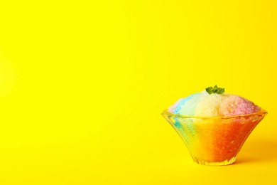 Photo of Rainbow shaving ice in glass dessert bowl on yellow background, space or text