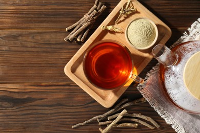 Photo of Aromatic licorice tea in cup, dried sticks of licorice root and powder on wooden table, flat lay. Space for text