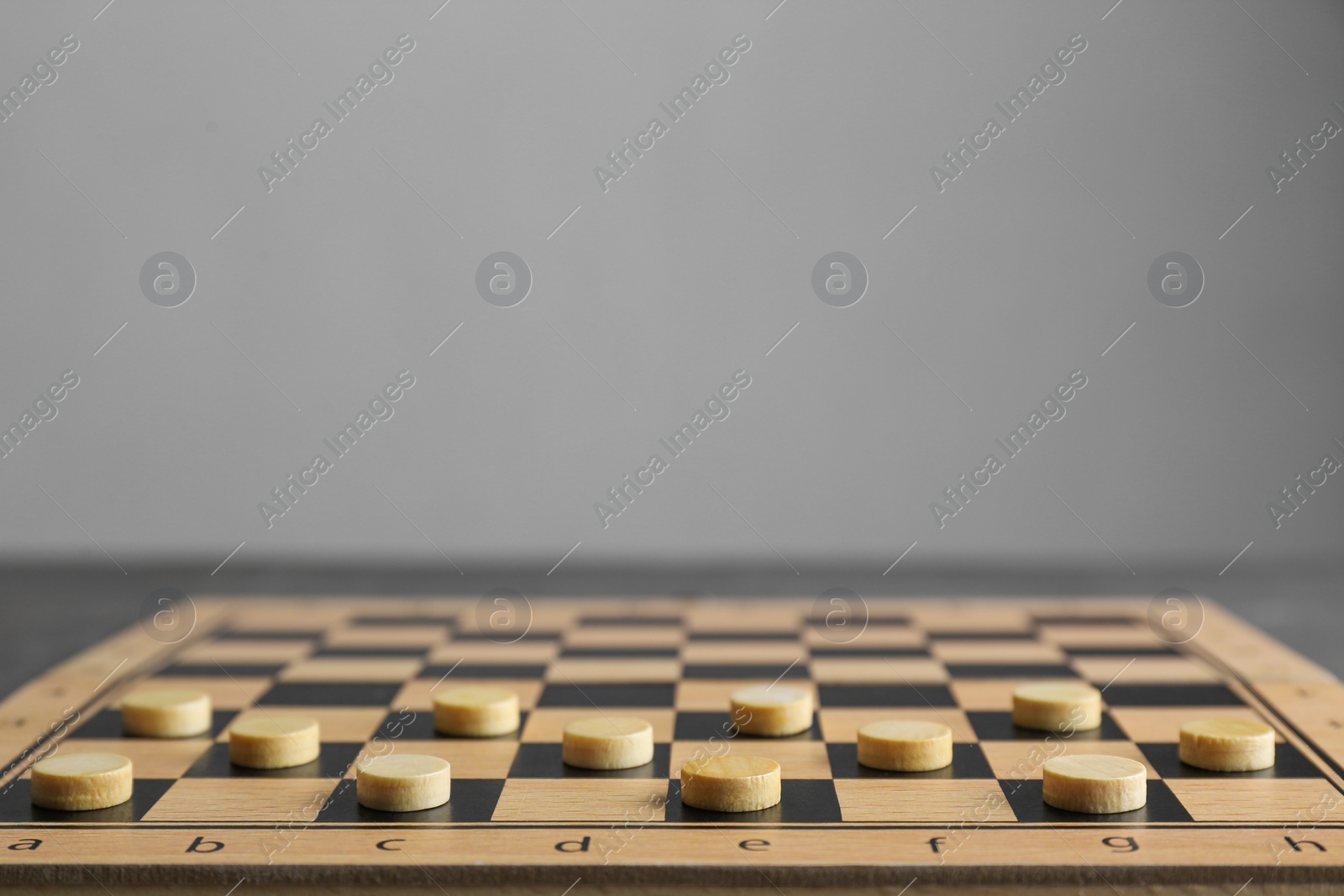 Photo of Wooden checkerboard with game pieces on light grey background, closeup. Space for text